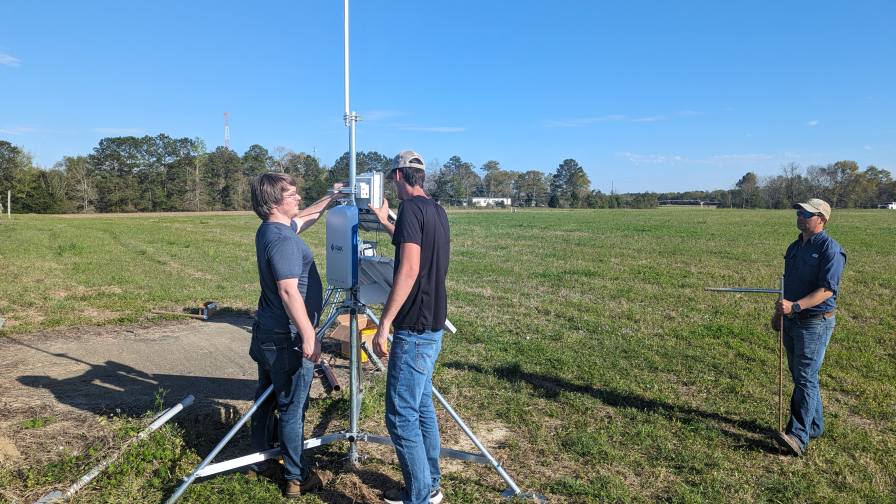 Iš kairės Andrew Balmosas, Joshas Bailey ir Derekas Hurley montuoja įrenginį ant savo SPRING trikojo viršaus. Ši sistema renka duomenis iš jutiklių, išdėstytų lauke, kad padėtų ūkininkams ir tyrėjams peržiūrėti realaus laiko duomenis iš savo laukų ar sodų, kad galėtų priimti valdymo sprendimus (Purdue universiteto / IoT4Ag nuotrauka).